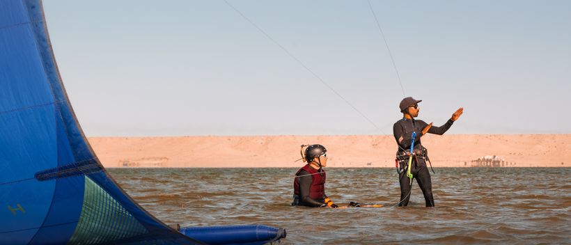 Kitelehrer begleitet einen Schüler im seichten Wasser der Lagune, der Kite in der Luft